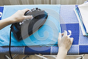 Woman`s hand ironing blue t-shirt on the ironing board.
