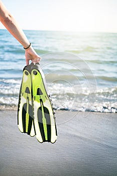 WomanÃÂ´s hand keep snorkel and swimming fins on a sandy beach. Water sports. Snorkeling. Travel and holiday concept.