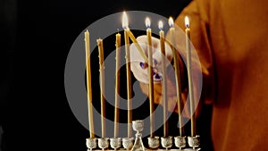 A woman's hand lights candles on the last day of Hanukkah from a shamash candle in a Hanukkah lamp