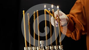 A woman's hand lights candles on the last day of Hanukkah from the shamash candle in the Hanukkah menorah