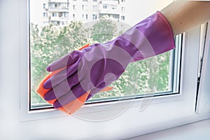 Woman`s hand in a lilac rubber glove wipes a glass unit window in a room with a rag