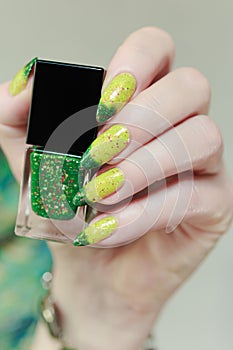 Woman\'s hand with long nails and bright yellow green thermo manicure