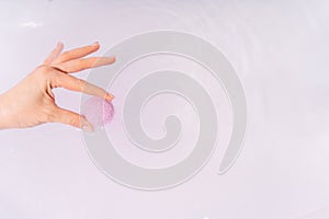 A woman& x27;s hand lowers a purple bath bomb into a bathtub of water
