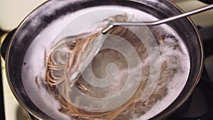 A woman's hand lowers spaghetti into boiling water in a saucepan