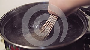 A woman's hand lowers spaghetti into boiling water in a saucepan