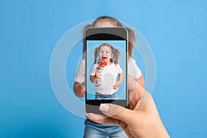 Woman`s hand making photo of a little girl with a mobile phone. Selective focus on a mobile phone with a portrait of a