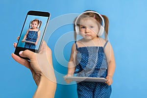 Woman`s hand making photo of a little girl with a mobile phone. Selective focus on a mobile phone with a portrait of a