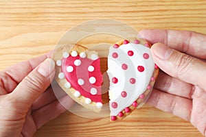 Woman's hand and man's hand holding two half heart shaped cookies attach on wooden background