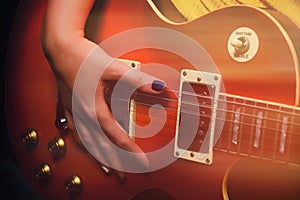 A woman`s hand with a manicure lies on the deck of a red electric guitar. Guitarist plays music in the recording Studio