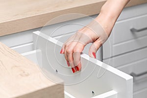 woman& x27;s hand with manicure opens a kitchen cabinet drawer.