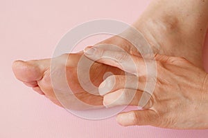 Woman`s hand massaging her bunion toes in bare feet to relieve pain on pink background Woman feet problem. Hallux valgus