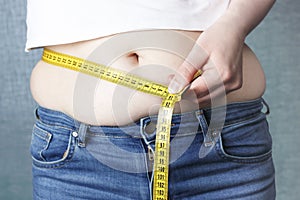 Woman`s hand measure her stomach with a tape measures, overweight concept