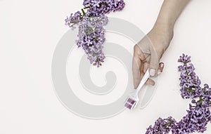 A woman`s hand with a mesoroller and lilac flowers on a white background. Concept of skin care, anti-wrinkle, Spa photo
