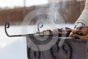 A woman\'s hand in a mitten fries a barbecue on the grill in nature on a sunny winter day. Selective focus