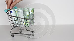 Woman`s hand moves trolley from supermarket with Stack of Euro banknotes. Money in shopping trolley. Online shopping or saving mon