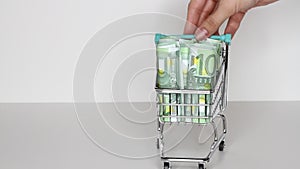 Woman`s hand moves trolley from supermarket with Stack of Euro banknotes. Money in shopping trolley. Online shopping or saving mon