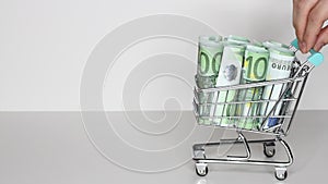 Woman`s hand moves trolley from supermarket with Stack of Euro banknotes. Money in shopping trolley. Online shopping or saving mon