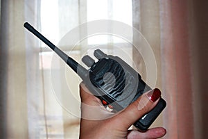 Woman`s hand with nail polish holds up a black transceiver in the house in front of the curtains