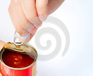 Woman`s hand opens lid of canned fish on white background. Sardine in tomato sauce. Processed food. Canned fish in tin can.