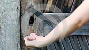 Woman`s hand opens an old wooden door with a metal key close-up