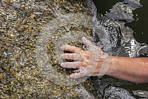 Woman`s hand out of the water trying to grab the coastal stone and escape from the sea.