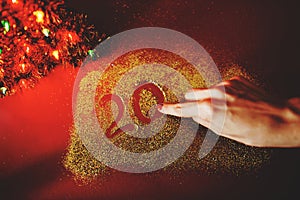 The woman`s hand paint the figure of 2020 in the claret background with sparkles. New Year`s concept