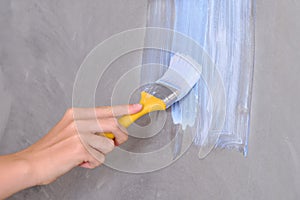 A woman`s hand paints the wall with a brush in white. Lifestyle repairs in the new apartment. Painting the walls yourself, girl