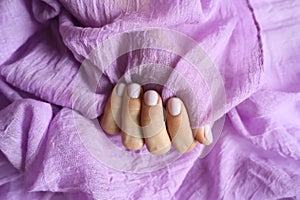 A woman`s hand with pale lilac nails and lilac cotton fabric