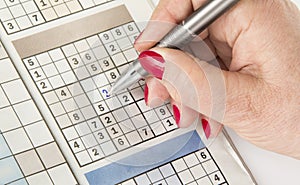 Woman`s hand with a pen is filling out sudoku