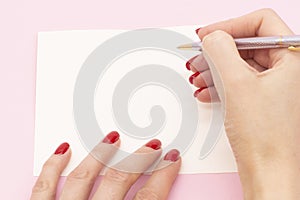 Woman`s hand with pen in position to write on blank white paper on a pink background