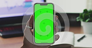 A woman's hand phone with green mock-up screen chroma key holds a smartphone of the workspace background. Stock