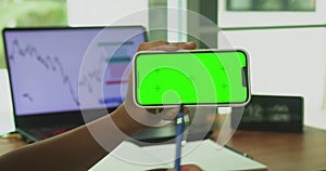 A woman's hand phone with green mock-up screen chroma key holds a smartphone of the workspace background. Stock
