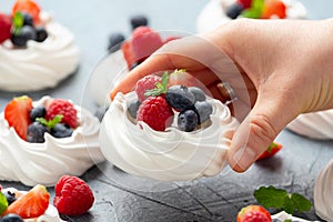 Woman`s Hand pick up meringue nest mini pavlova cake with fresh berries strawberry blueberry raspberry and mint for healthy deser