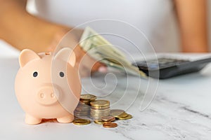 a woman\'s hand with a piggy bank and a calculator on the office table. paper dollars and coins savings, inflation.