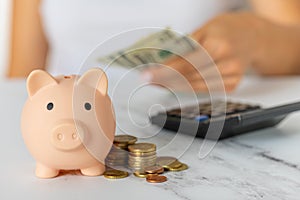 a woman's hand with a piggy bank and a calculator on the office table. paper dollars and coins savings, inflation.