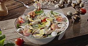 A woman`s hand pins with a fork chicken fillet, tomato, shpinach in a plate with salad with quail eggs, chicken fillet