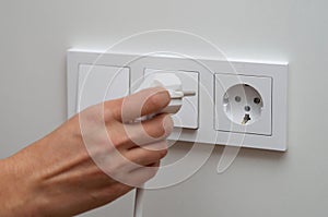 Woman's hand plugs an electric plug into a socket