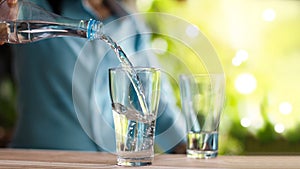 Woman`s hand pouring drinking water from bottle into glass