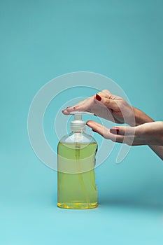 A woman`s hand pouring liquid soap on blue background