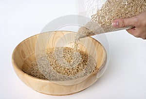 Woman`s hand is pouring raw brown rice packed in a plastic bag onto a wooden bowl