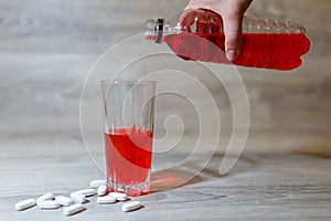 A woman's hand pours a red sports drink or lemonade into a glass Cup from a plastic bottle. Energy drink in glass and plastic bot