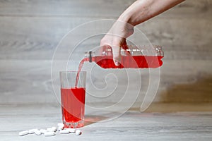 A woman's hand pours a red sports drink or lemonade into a glass Cup from a plastic bottle. Energy drink in glass and plastic bot