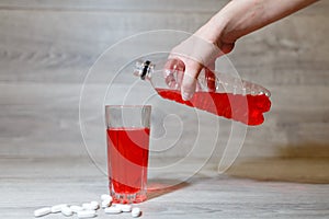 A woman's hand pours a red sports drink or lemonade into a glass Cup from a plastic bottle. Energy drink in glass and plastic bot