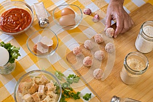 Woman`s hand preparing fresh meatballs ready to be cooked, wooden cutting board and raw ingredients