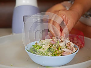 A woman`s hand preparing / putting food ingredients in a small bowl for blending for cooking food at home