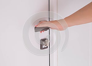 A woman`s hand presses the handle of a modern white door to a room. Opening an interior door, close-up