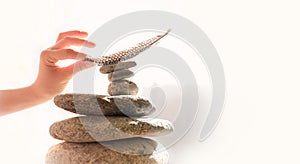 Woman`s hand put a feather on a pyramid of stones. Equilibrium, Balance concept. Zen stones on white