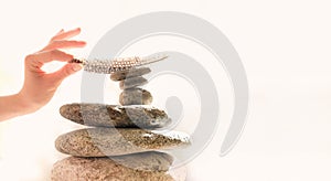 Woman`s hand put a feather on a pyramid of stones. Equilibrium, Balance concept. Zen stones on white