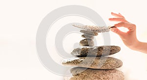 Woman`s hand put a feather on a pyramid of stones. Equilibrium, Balance concept. Zen stones on white