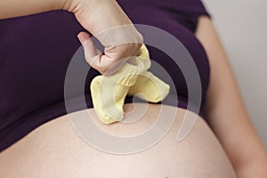 Woman`s hand put on her fingers little baby socks and walks, make step on belly, pregnant woman on gray background